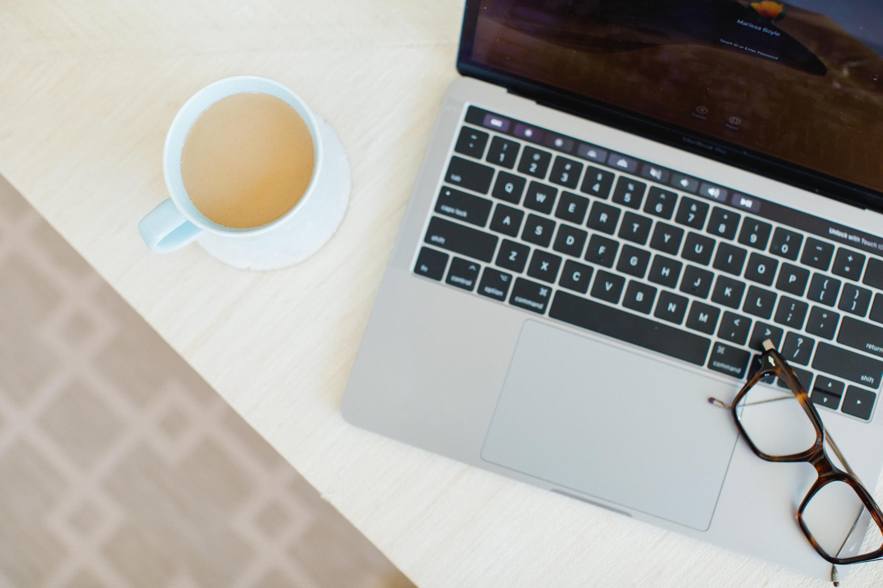 A cup of tea sitting next to an open laptop on a desk